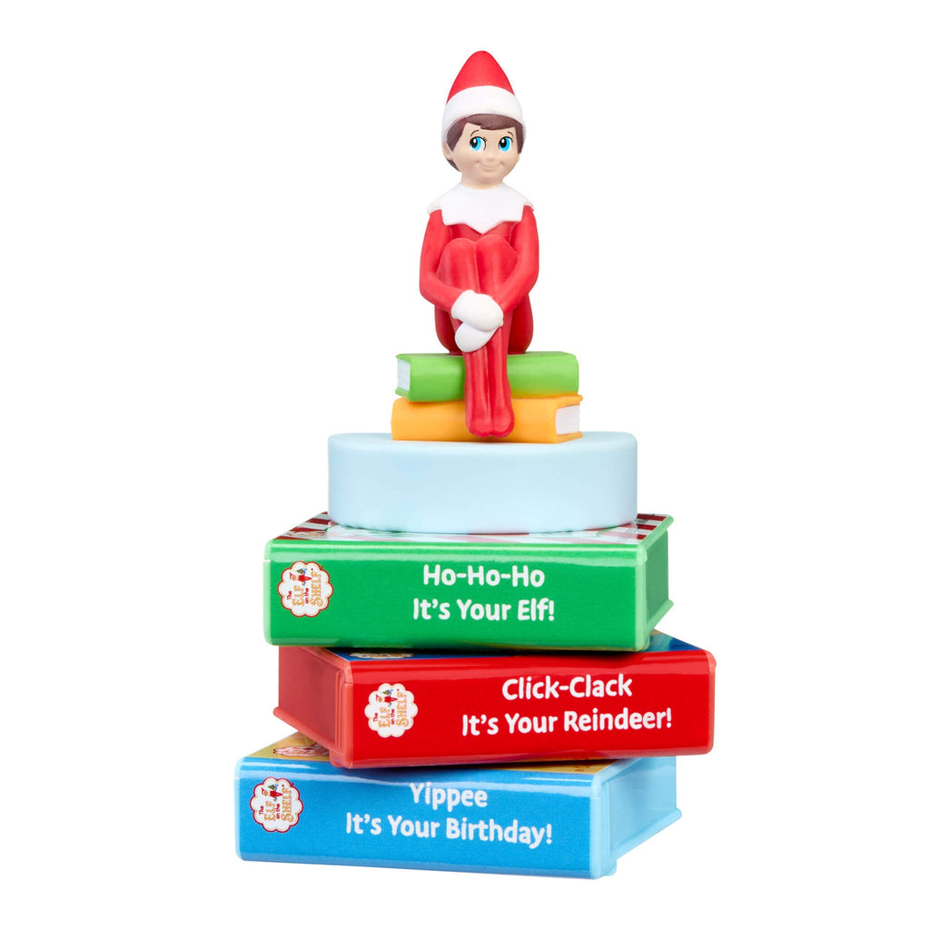 Elf on the shelf figurine sitting on a stack of colorful books with text