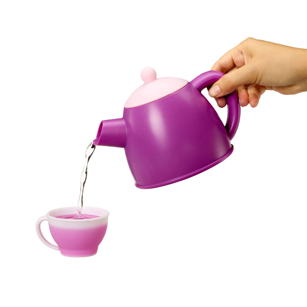 Purple teapot with pink interior being filled with tea from a hand on a white background