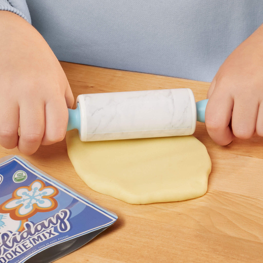 Child rolling out play dough with a roller on a wooden surface