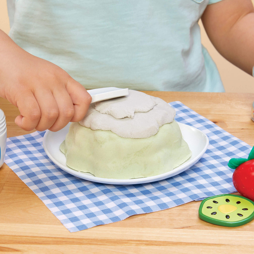 Child putting pretend frosting on cake on a checkered tablecloth